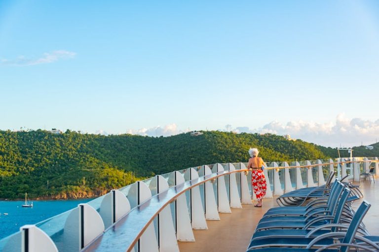 Senior woman enjoying a serene view from a cruise ship deck, surrounded by lush hills and ocean.